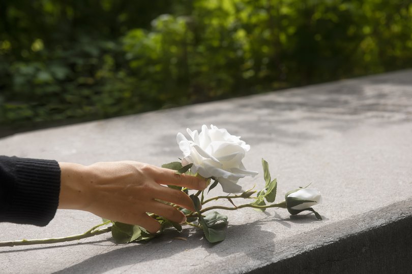 Une main qui pose une rose blanche sur une pierre tombale